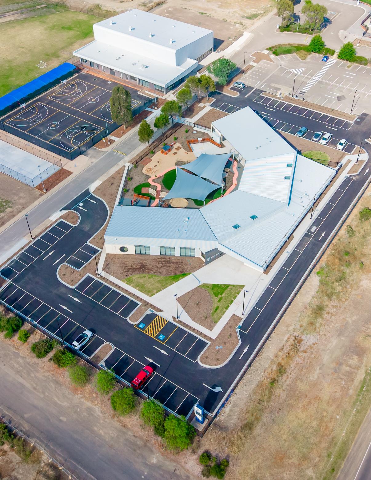 Aerial view of a commercial school complex with shaded play area, basketball courts and parking